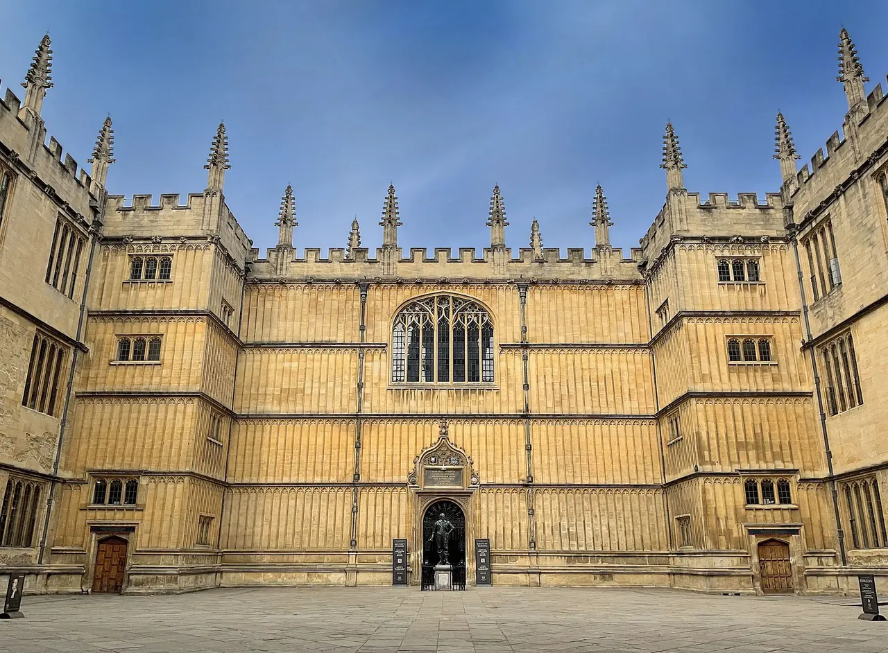 Der Old Schools Quadrangle der Bodleian, honigfarbene Steinflügel um einen gepflasterten Innenhof unter blauem Himmel