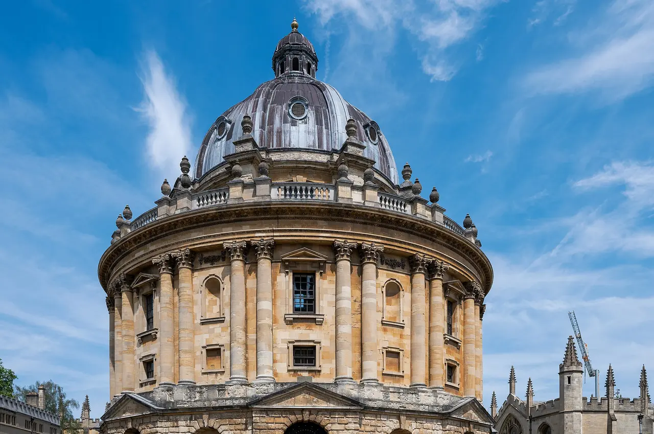 Die Radcliffe Camera, eine runde Kuppelbibliothek aus goldenem Stein, vor blauem Himmel